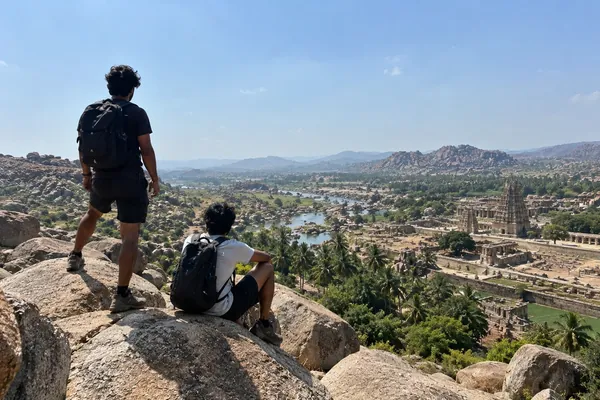 Two friends rest on granite boulders above Hampi, the Tungabhadra river and temple ruins spread out below